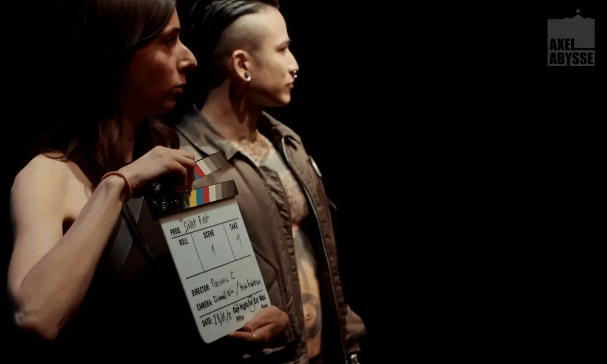 Axel Abysse behind the scenes: two performers holding a production clapperboard